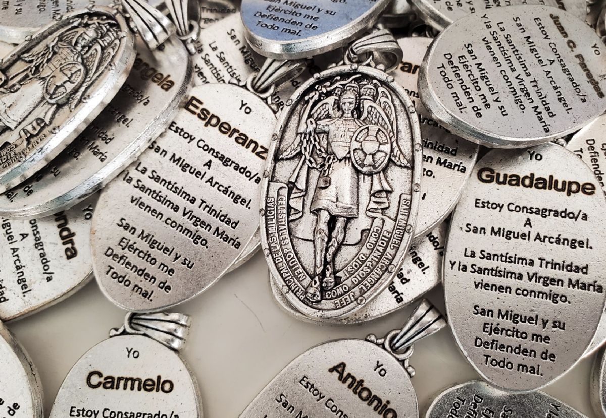 Pile of silver Saint Michael medals, each engraved on the back with a person's name and a prayer in Spanish
