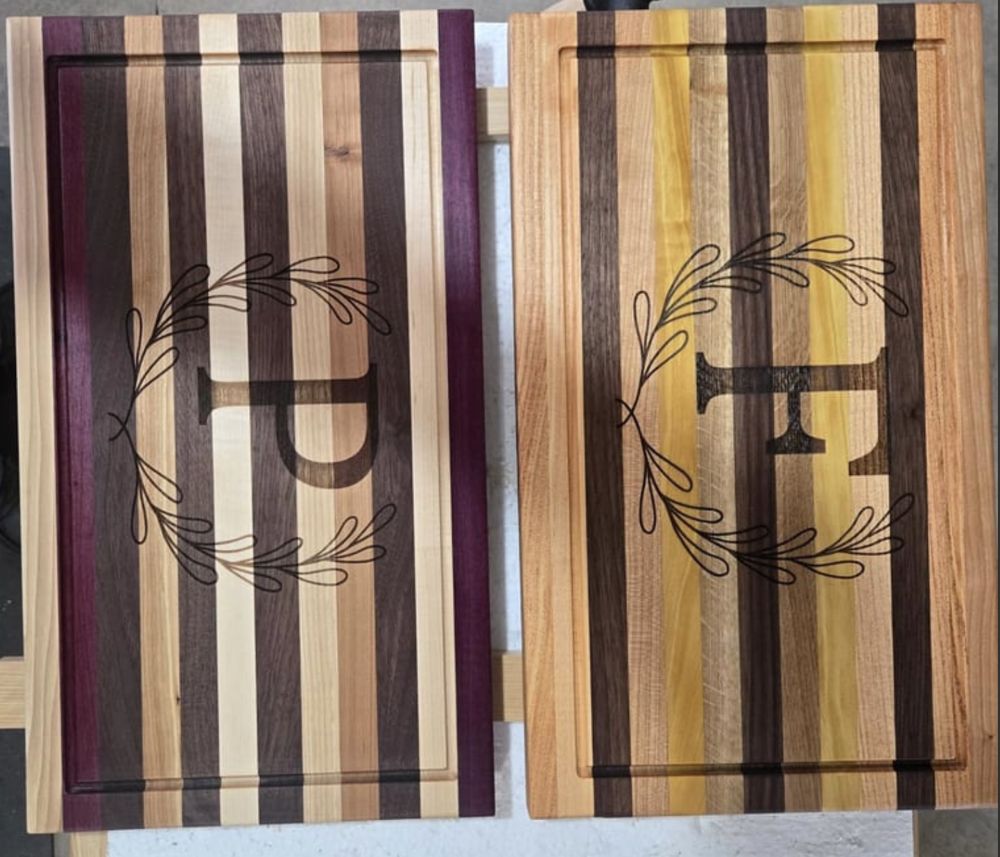 Two striped hardwood cutting boards engraved with monogram initials inside a leaf wreath